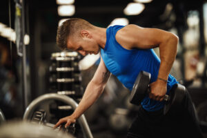 A muscular guy in sportswear working out at the gym, pumping up his back muscles with heavy weights.