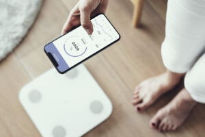 Woman using health tracking on her phone by the weighing scale