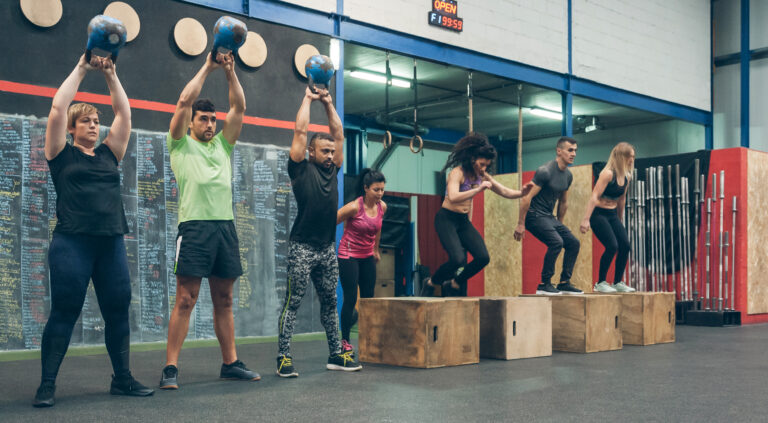 Group of athletes performing kettlebell exercises and box jumps in a workout session