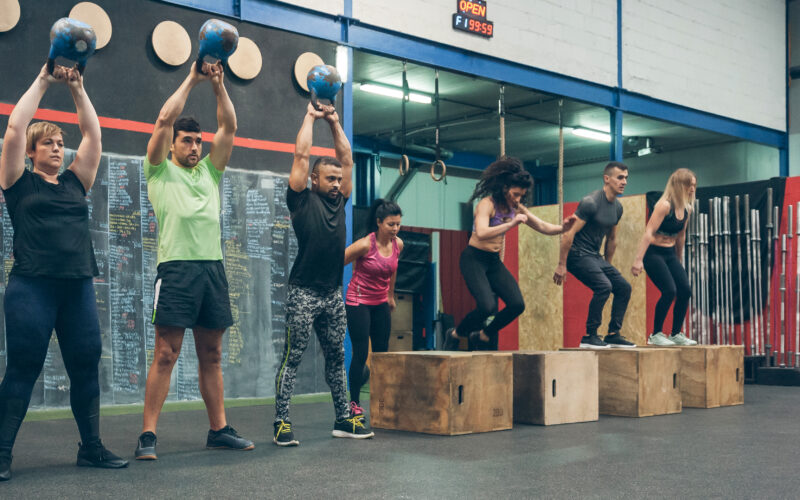 Group of athletes performing kettlebell exercises and box jumps in a workout session