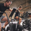 A man and a woman on assault bikes performing concurrent training.