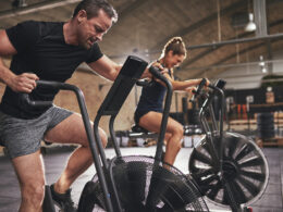 A man and a woman on assault bikes performing concurrent training.