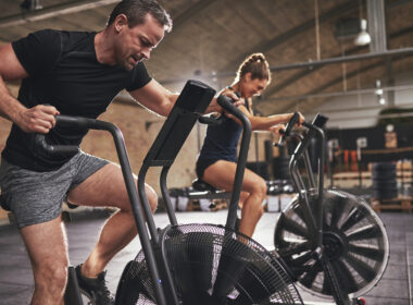 A man and a woman on assault bikes performing concurrent training.