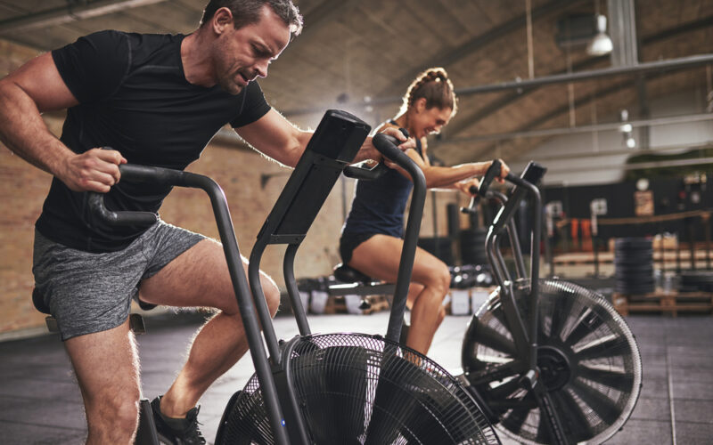 A man and a woman on assault bikes performing concurrent training.